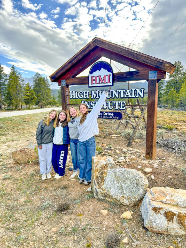 Four girls smiling in front of the High Mountain Institute sign